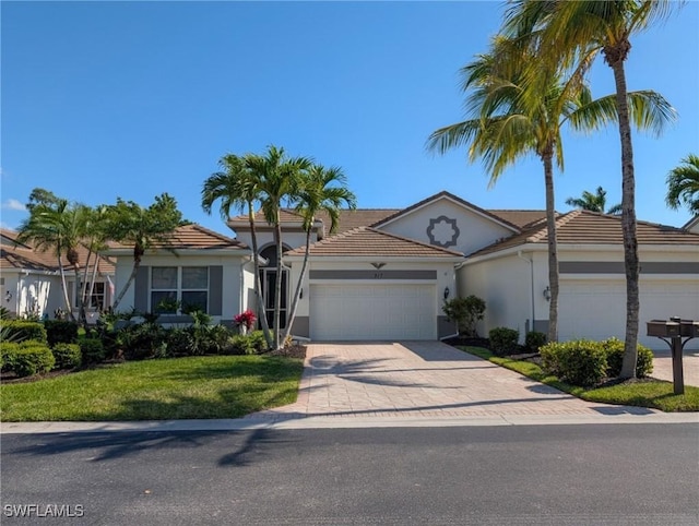 single story home with stucco siding, a garage, driveway, a tile roof, and a front lawn