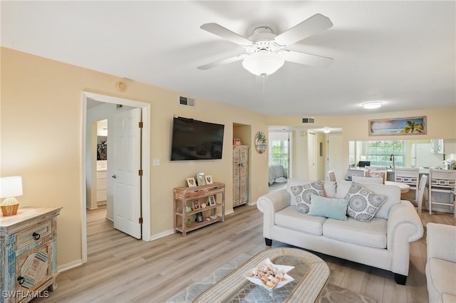 living area with light wood finished floors, a ceiling fan, and baseboards
