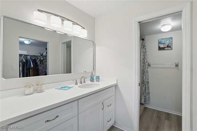bathroom with vanity, wood finished floors, a walk in closet, and baseboards