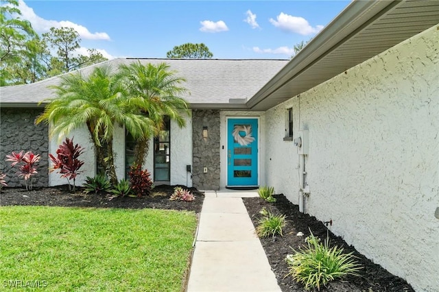 doorway to property featuring stucco siding, a yard, and stone siding