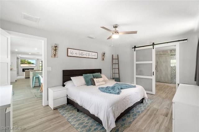 bedroom featuring a barn door, light wood-type flooring, recessed lighting, ceiling fan, and baseboards