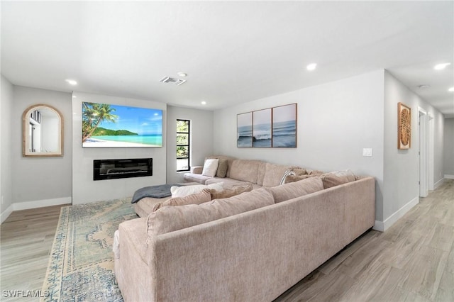 living area featuring baseboards, light wood finished floors, recessed lighting, and a glass covered fireplace