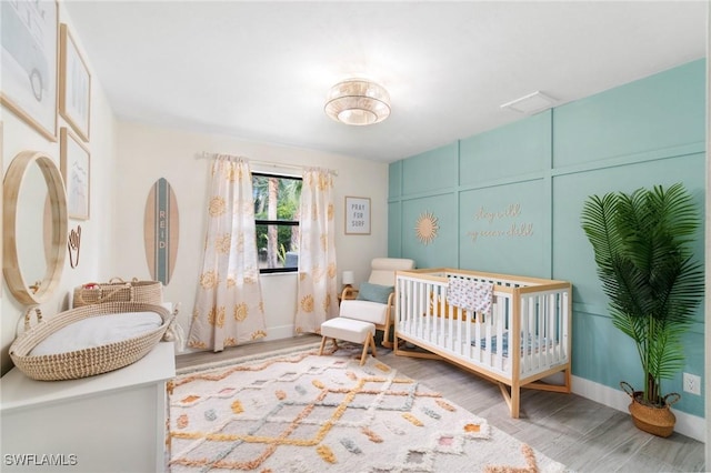 bedroom featuring wood finished floors, a crib, and baseboards