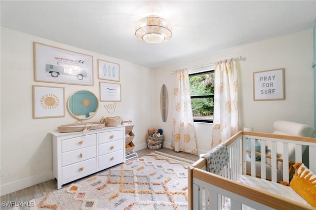 bedroom with wood finished floors, a nursery area, and baseboards
