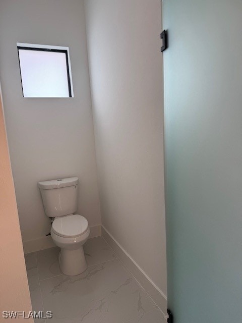 bathroom with toilet, baseboards, and marble finish floor