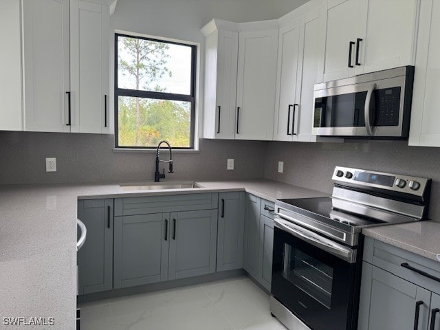 kitchen featuring a sink, stainless steel appliances, white cabinetry, tasteful backsplash, and marble finish floor