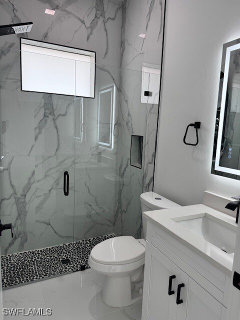 full bath with vanity, toilet, a marble finish shower, and marble finish floor