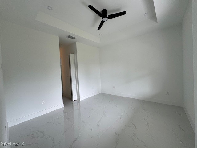 empty room featuring a ceiling fan, a tray ceiling, baseboards, marble finish floor, and visible vents
