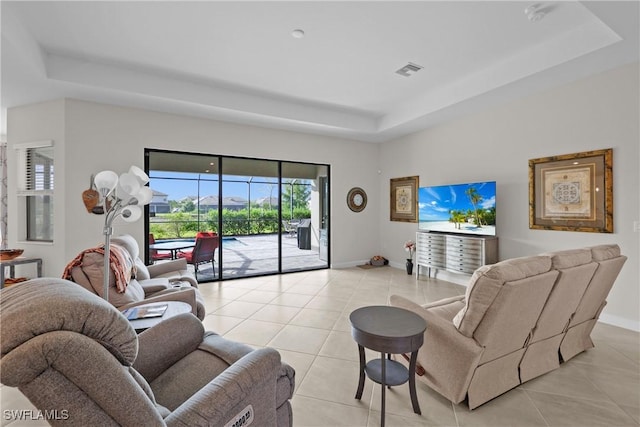 living room with a tray ceiling, light tile patterned flooring, baseboards, and visible vents