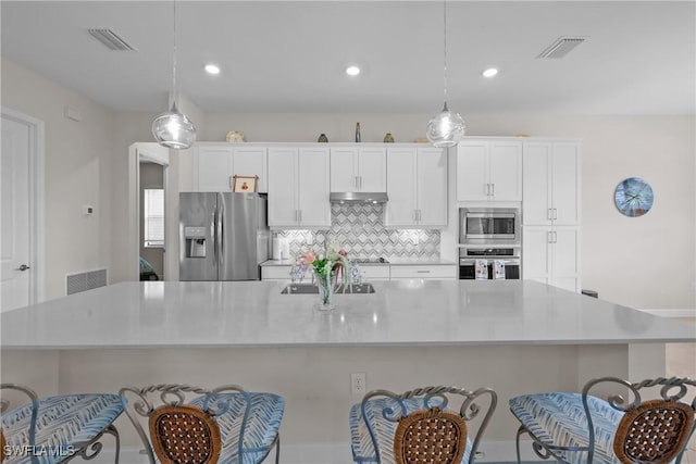 kitchen with white cabinetry, a large island with sink, under cabinet range hood, appliances with stainless steel finishes, and decorative backsplash