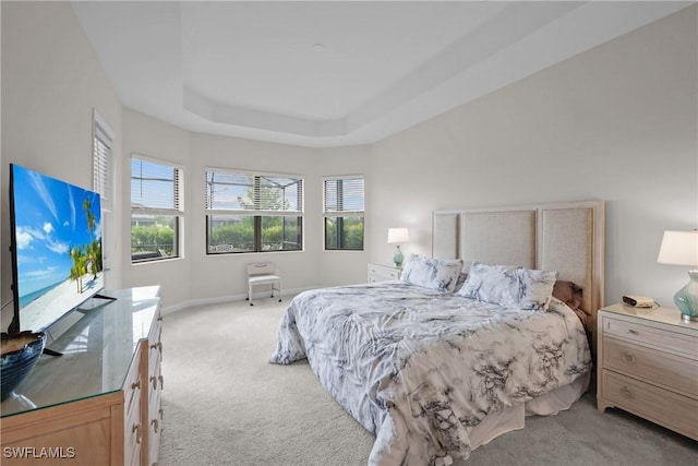 bedroom featuring light colored carpet, multiple windows, baseboards, and a tray ceiling