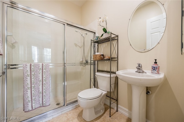 bathroom featuring toilet, a stall shower, tile patterned floors, baseboards, and a sink