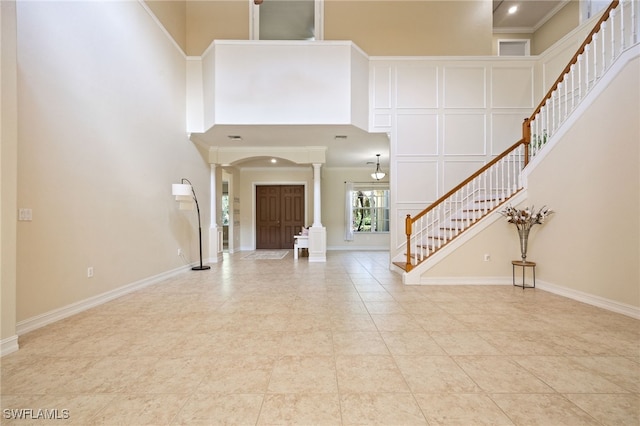 foyer featuring decorative columns, a towering ceiling, stairway, arched walkways, and baseboards