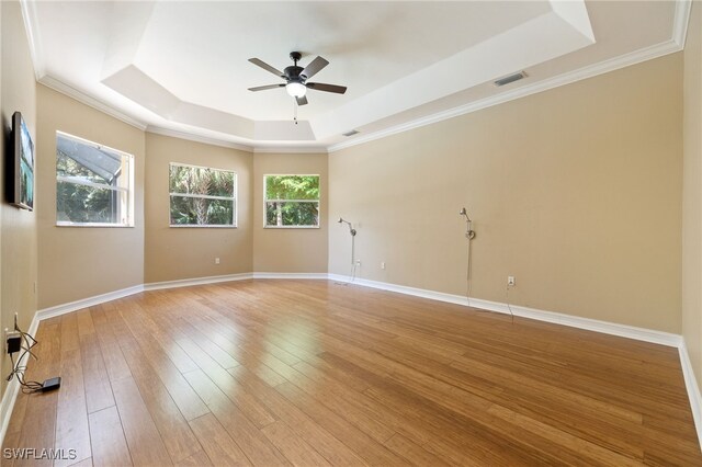 unfurnished room with a raised ceiling, a ceiling fan, light wood-style floors, baseboards, and ornamental molding