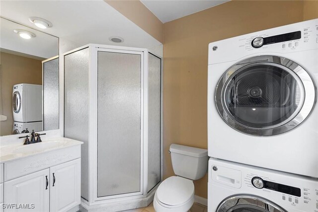 bathroom with stacked washer / dryer, a shower stall, toilet, and vanity