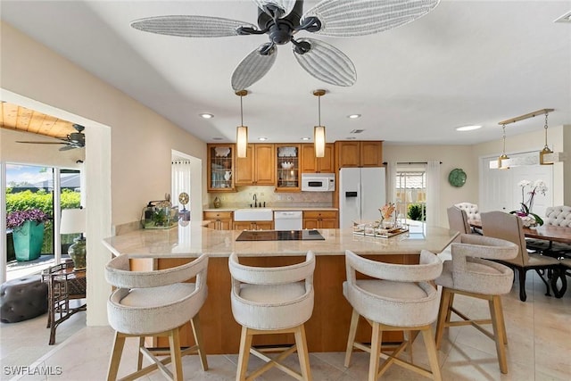 kitchen with white appliances, ceiling fan, brown cabinets, a sink, and glass insert cabinets
