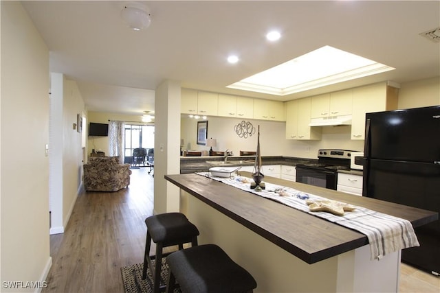 kitchen featuring black appliances, under cabinet range hood, butcher block counters, a kitchen breakfast bar, and baseboards