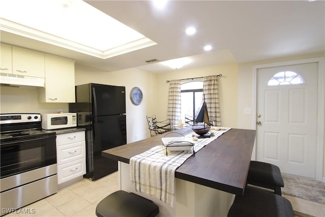 kitchen with stainless steel electric stove, freestanding refrigerator, white microwave, under cabinet range hood, and light tile patterned flooring