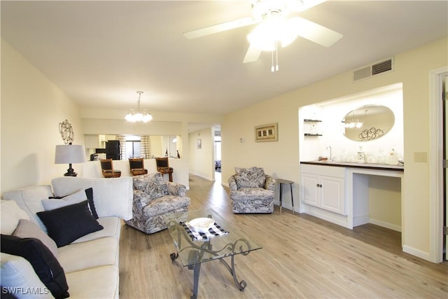 living room featuring a chandelier, light wood finished floors, ceiling fan, bar area, and baseboards