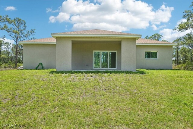 back of house featuring stucco siding and a lawn
