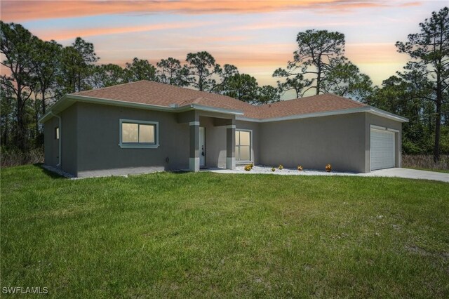 view of front facade featuring stucco siding, an attached garage, a front lawn, concrete driveway, and a shingled roof