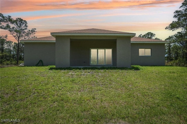 back of house at dusk with stucco siding and a yard