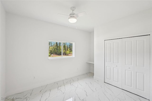 unfurnished bedroom with marble look tile flooring, a closet, and a ceiling fan