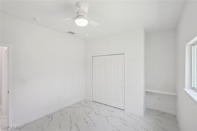 unfurnished bedroom with light marble finish flooring, a closet, ceiling fan, and baseboards