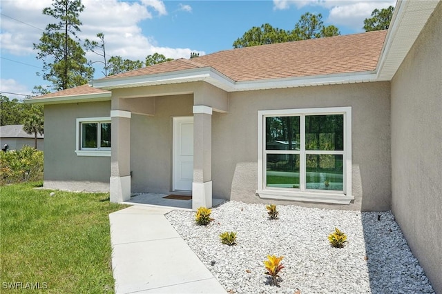 property entrance featuring stucco siding, a shingled roof, and a lawn
