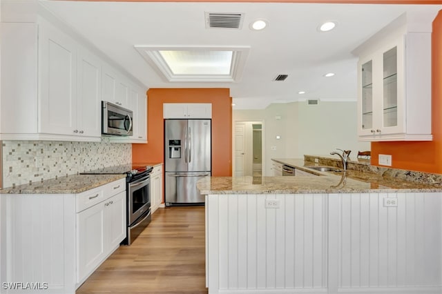 kitchen featuring stainless steel appliances, a sink, a peninsula, glass insert cabinets, and light stone counters