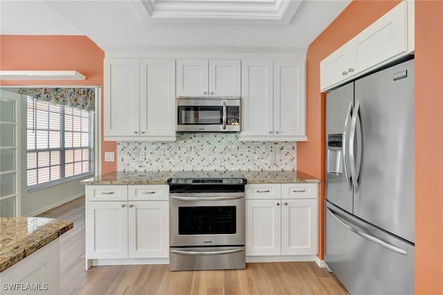 kitchen with stainless steel appliances, a tray ceiling, light wood-type flooring, white cabinets, and crown molding