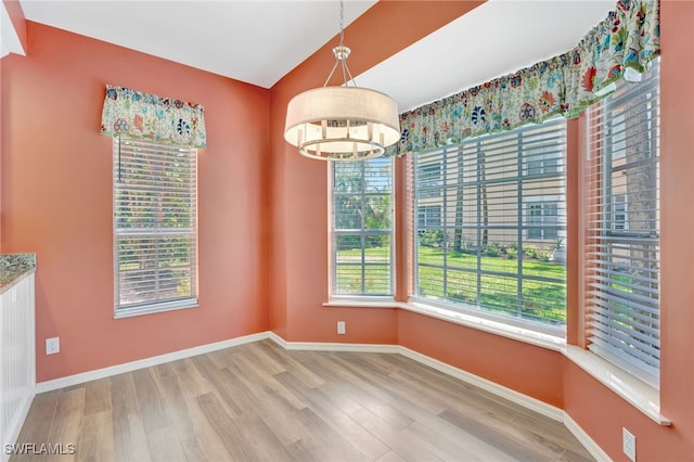 unfurnished dining area featuring wood finished floors, a chandelier, and baseboards