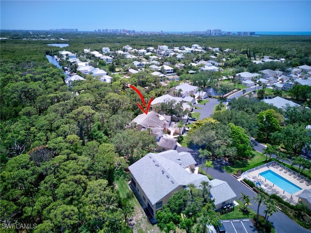 aerial view of property and surrounding area featuring a heavily wooded area, a pool, and a nearby body of water