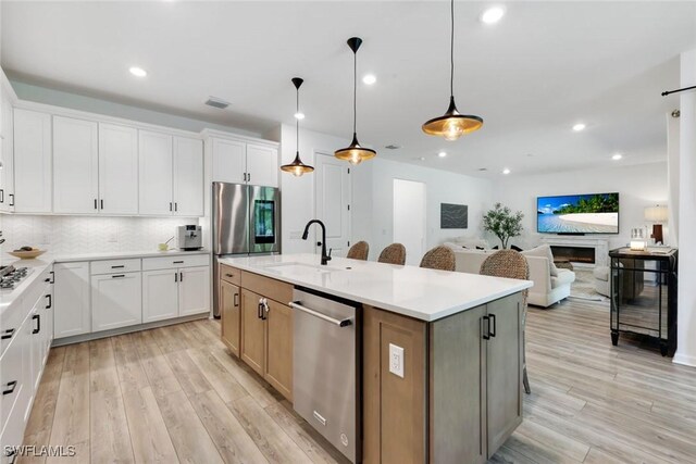 10427 Ventana Ln, Naples, FL 34120 - kitchen featuring stainless steel appliances, a sink, light wood finished floors, a kitchen island with sink, and backsplash