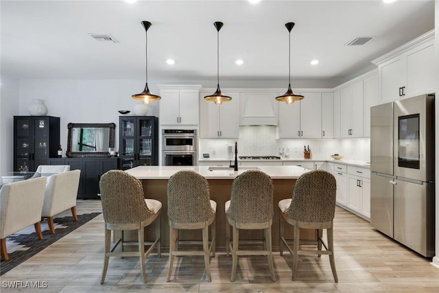 10427 Ventana Ln, Naples, FL 34120 - kitchen with stainless steel appliances, custom range hood, light countertops, white cabinets, and a center island with sink