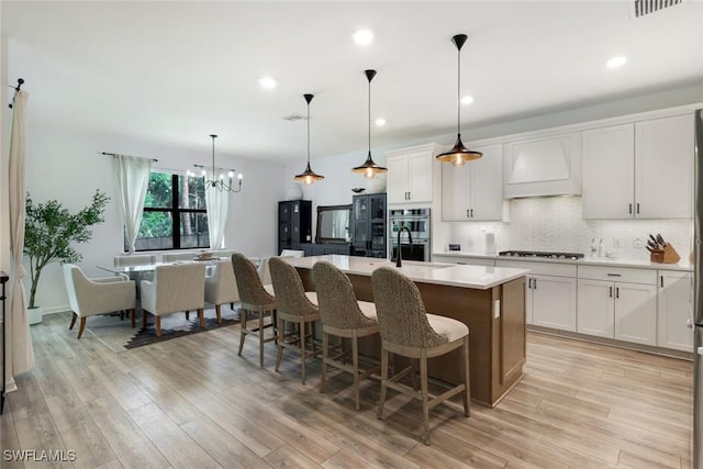10427 Ventana Ln, Naples, FL 34120 - kitchen with custom exhaust hood, stovetop, light countertops, a kitchen island with sink, and a chandelier