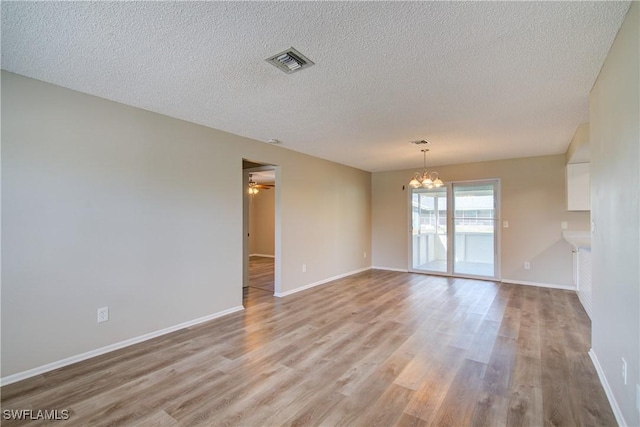 spare room featuring a chandelier, a textured ceiling, light wood-style flooring, baseboards, and a ceiling fan