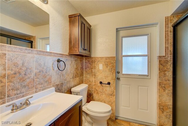 bathroom with tile walls, toilet, vanity, and wainscoting