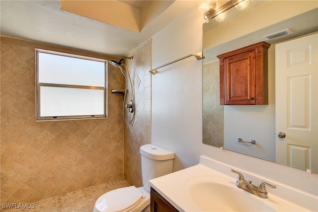 bathroom featuring toilet, tiled shower, and vanity