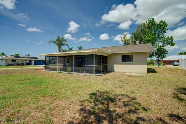 back of property featuring a sunroom, a lawn, and stucco siding