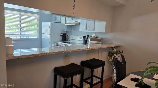 kitchen featuring white appliances, under cabinet range hood, white cabinets, a kitchen breakfast bar, and wood finished floors