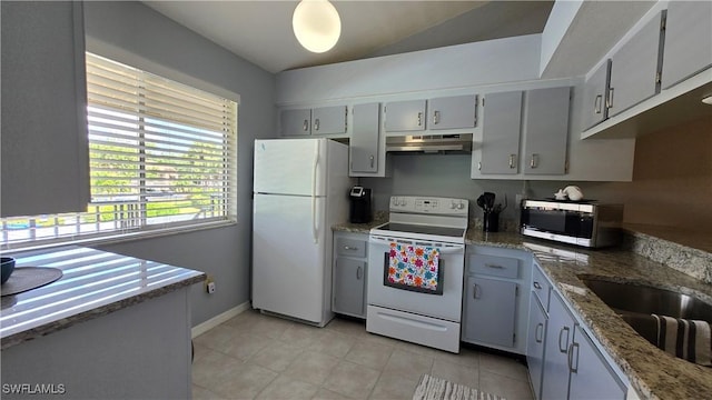 kitchen with white appliances, under cabinet range hood, a sink, light tile patterned floors, and light stone counters