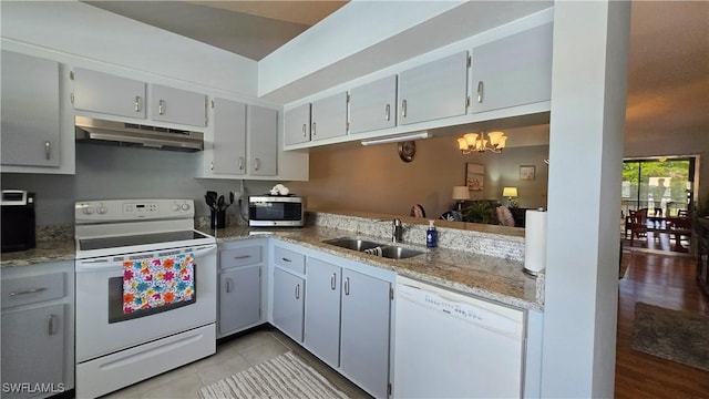 kitchen with under cabinet range hood, white appliances, a sink, a chandelier, and light stone countertops