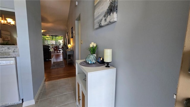 hallway featuring light tile patterned floors, a chandelier, and baseboards