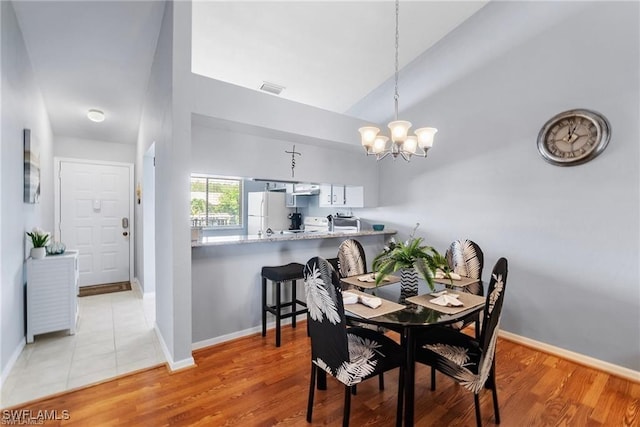 dining space featuring a chandelier, baseboards, lofted ceiling, and light wood-style floors