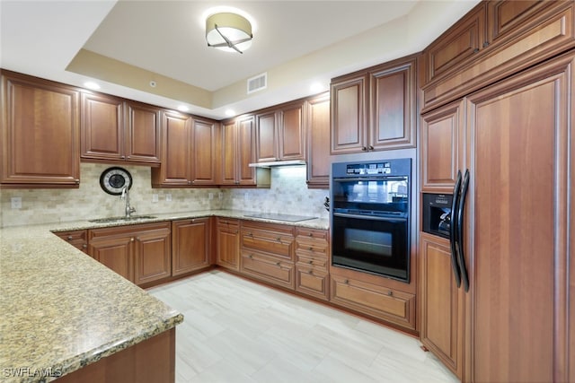 kitchen with black appliances, a sink, backsplash, light stone countertops, and brown cabinetry