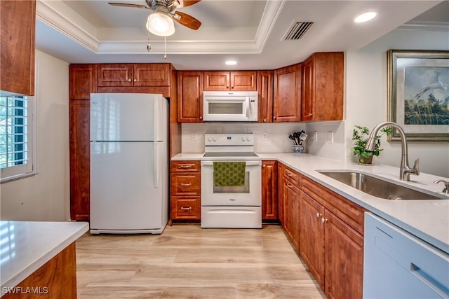 kitchen featuring white appliances, a sink, a raised ceiling, a ceiling fan, and light wood-type flooring