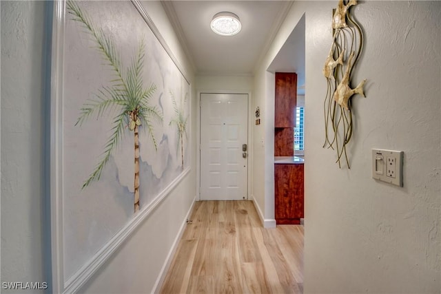 hall featuring light wood-type flooring, crown molding, and baseboards
