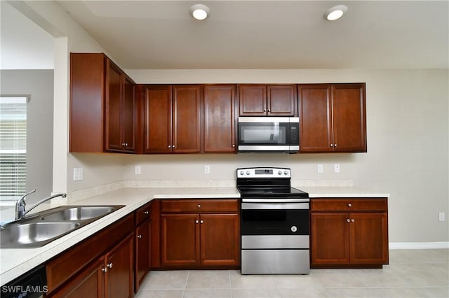 kitchen with stainless steel appliances, a sink, light countertops, and light tile patterned floors