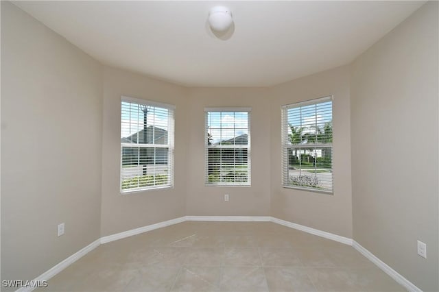 spare room featuring healthy amount of natural light, light tile patterned floors, and baseboards